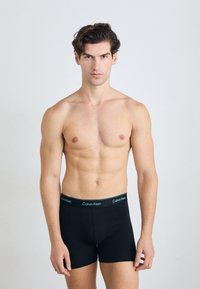 Fekete boxer alsónadrág puha, rugalmas derékháttal, melyen kontrasztos színű "Calvin Klein" logó található. Sima anyag, testhezálló fazon.