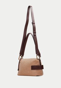 Sac en faux shearling beige avec une bandoulière en cuir texturé brun ; doté de quincaillerie dorée et d'un logo en relief proéminent sur le côté.