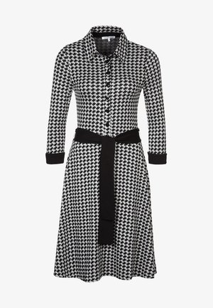 Schwarz-weiß kariertes Hahnentrittmuster-Kleid mit Kragen, durchgehender Knopfleiste, langen Ärmeln und einem schwarzen Stoffgürtel in der Taille.