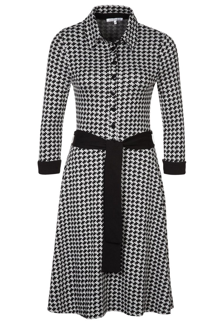 Robe à motif pied-de-poule noir et blanc avec col, boutonnage intégral sur le devant, manches longues et ceinture en tissu noir à la taille.