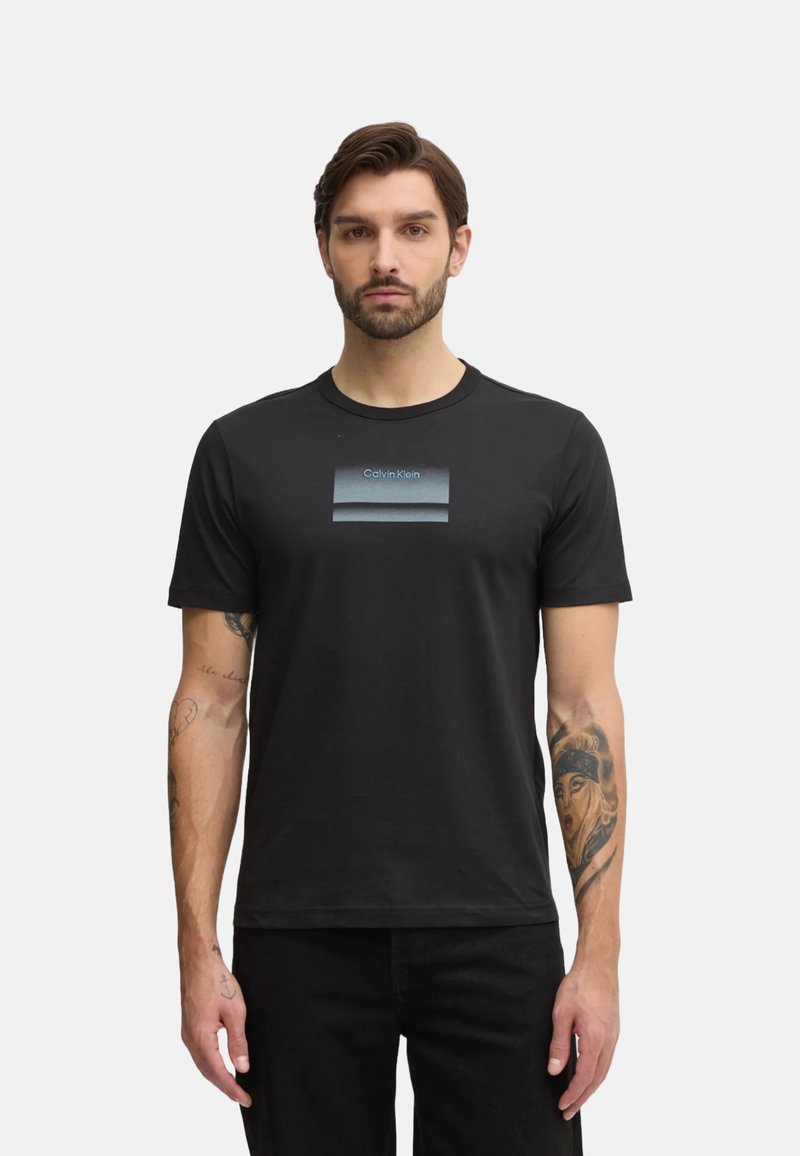 Camiseta de algodón negra con una franja horizontal azul en degradado que presenta el texto "Calvin Klein" en el centro. Diseño de manga corta y cuello redondo.
