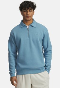 Svetlo modra pulover s kapuco in zadrgo, izdelan iz mehkega materiala. Ima diskreten logotip na prsih in rebraste manšete.