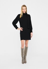 Abito nero a maniche lunghe con collo alto e vestibilità slim, abbinato a stivali texture a stampa serpente al ginocchio in tonalità beige e grigio.