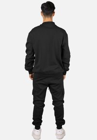 Sudadera ajustada negra y pantalones cargo hechos de tela lisa. Presentan puños acanalados y bolsillos con cremallera, con una silueta relajada.