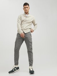 Light beige button-up shirt, gray cargo pants with side pockets, green sneakers with white accents. Simple design and relaxed fit.