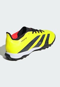 Chaussure de football synthétique jaune avec des rayures noires et grises, semelle intermédiaire blanche et crampons texturés. Présente un design lacé noir et un intérieur rouge.