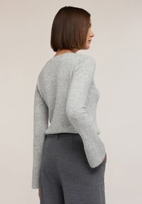 Grå texturerad tröja med lång ärm, rund halsringning och avslappnad passform, matchad med mörkgrå skräddarsydda byxor. Bakgrunden är neutral.