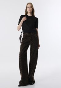 Top corto nero a maniche corte con logo in rilievo, abbinato a pantaloni a gamba larga con stampa leopardo marrone. L'outfit presenta un tessuto morbido e una vestibilità casual.