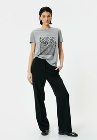 Grå bomulds t-shirt med grafisk tryk. Sammen med sorte brede bukser og skinnende sorte sko. Enkel design og behagelig pasform.