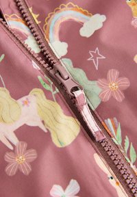 Tessuto rosa chiaro con zipper, caratterizzato da unicorni, arcobaleni, fiori e stelle. La cerniera è marrone chiaro con un tirante decorativo.