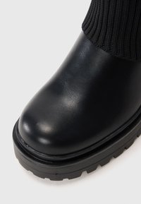 Black leather ankle boot with a rounded toe, textured fabric detailing at the top, and a chunky rubber sole for traction.
