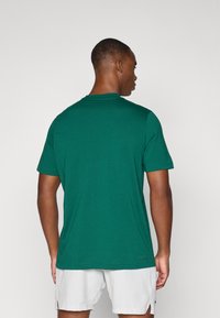 T-shirt verde de manga curta, feito de tecido suave, com gola redonda e corte reto, apresentando um logótipo discreto perto da bainha.