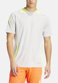 Lichtgrijze sportshirt met korte mouwen, voorzien van gele accenten en een gestructureerd patroon aan de voorkant. Gemaakt van ademend materiaal.