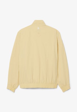 Beige lichtgewicht jas met lange mouwen, geribde manchetten en zoom, en een klein wit logo gecentreerd vlak bij de bovenste achterkant van de kraag.