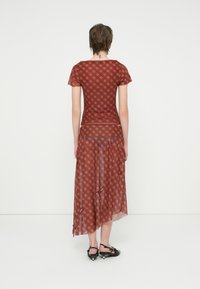 Punainen ja ruskea kuviollinen mekko lyhyillä hihoilla ja valuvahelma, jossa on läpinäkyvä päällyskangas ja solmittu yksityiskohta helman kohdalla.