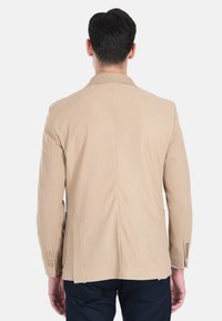 Blazer beige con una texture a rilievo, con un ventaglio posteriore singolo e due tasche laterali. Presenta polsini con bottoni e una silhouette su misura.