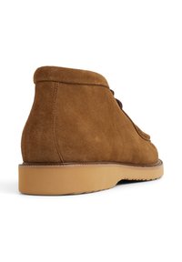 Bottes ankle en suede marron avec un bout arrondi, un design lacé et une surface texturée. Elles disposent d'une semelle en caoutchouc beige et de coutures décoratives.