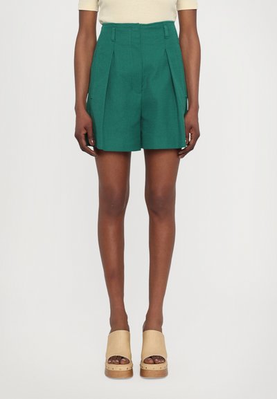 Shorts taille haute teal avec des plis, en tissu texturé, dotés de poches latérales. Associés à des sabots en plateforme beige.