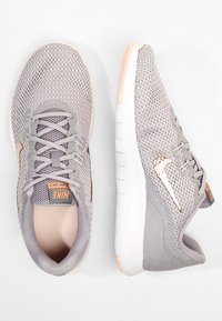 Buty do biegania Nike w jasnoszarej siateczce z ciemniejszymi szarymi akcentami, wyposażone w wyściełane wnętrze, sznurowane zapięcie oraz teksturowaną podeszwę. Detal logo w kolorze różowego złota.