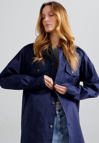Donkerblauwe lange mouwen shirtjack gemaakt van gladde stof, met twee borstzakken, knoopsluitingen en een relaxte pasvorm.