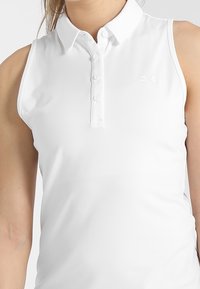 Bílá bezrukávová polo košile s klasickým límečkem, zapínáním na knoflíky a malým logem na prsou. Hladká, lehká látka.