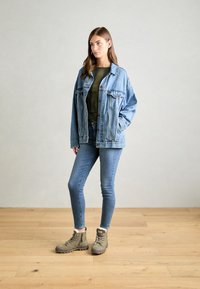 Denimjakke med løs passform, lyseblå farge, to framlommer; olivengrønn topp; tettsittende blå jeans; grå ankelstøvler med snøring.