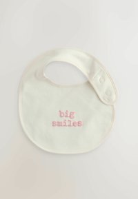 Bomullshak i off-white med rund form, med broderad rosa text som säger "stora leenden." Två tryckknappar på sidan.