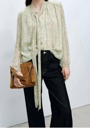 Bloes met bloemenpatroon in lichtgroen met knoopsluiting aan de voorkant en strikjes; gecombineerd met brede broekspijpen van donker denim en een bruine suède schoudertas.
