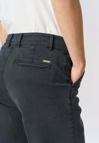 Pantaloni neri dalla texture liscia, con una tasca posteriore e un dettaglio argentato con il marchio sopra la tasca destra.