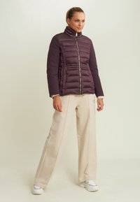 Chaqueta de plumas morada con un cuello alto, cierre de cremallera y bolsillos laterales. Combinada con pantalones de pierna ancha color crema y zapatillas blancas.