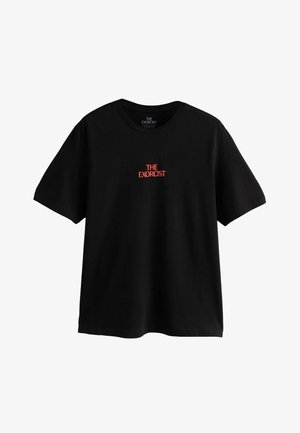 Czarna bawełniana koszulka z krótkim rękawem i okrągłym dekoltem. Z przodu, na środku, znajduje się napis "THE EXORCIST" w kolorze czerwonym.