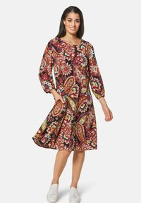 Langärmliges A-Linie-Kleid mit einem schwarzen, roten und mehrfarbigen Paisleymuster. Hergestellt aus leichtem Stoff; hat einen runden Ausschnitt.