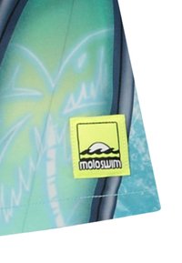 Peldbikses zilā krāsā ar tropisku rakstu. Tām ir zaļa birka ar melnu tekstu, logo un viļņu dizainu.