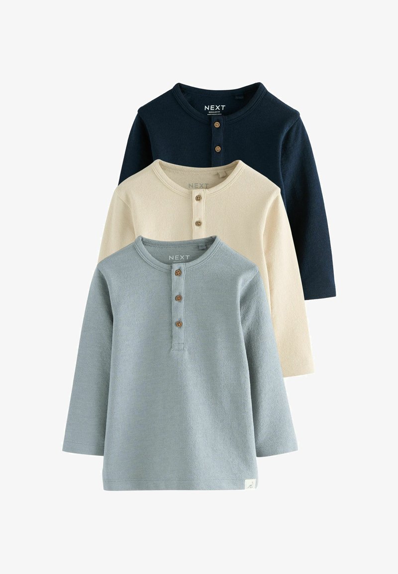 Trois hauts henley à manches longues en bleu marine, crème et bleu clair, chacun avec un col rond et trois boutons en bois, empilés verticalement.