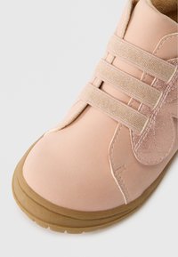 Světlé růžové tenisky s hladkou strukturou, s elastickými pásky pro uzavření a tan gumovou podrážkou, doplněné o jemný lesk.