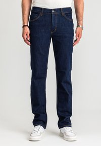 Ciemnoniebieskie dżinsy o prostym kroju, z pomarańczowymi przeszyciami i pięcioma kieszeniami, zestawione z białymi trampkami dla kontrastu.