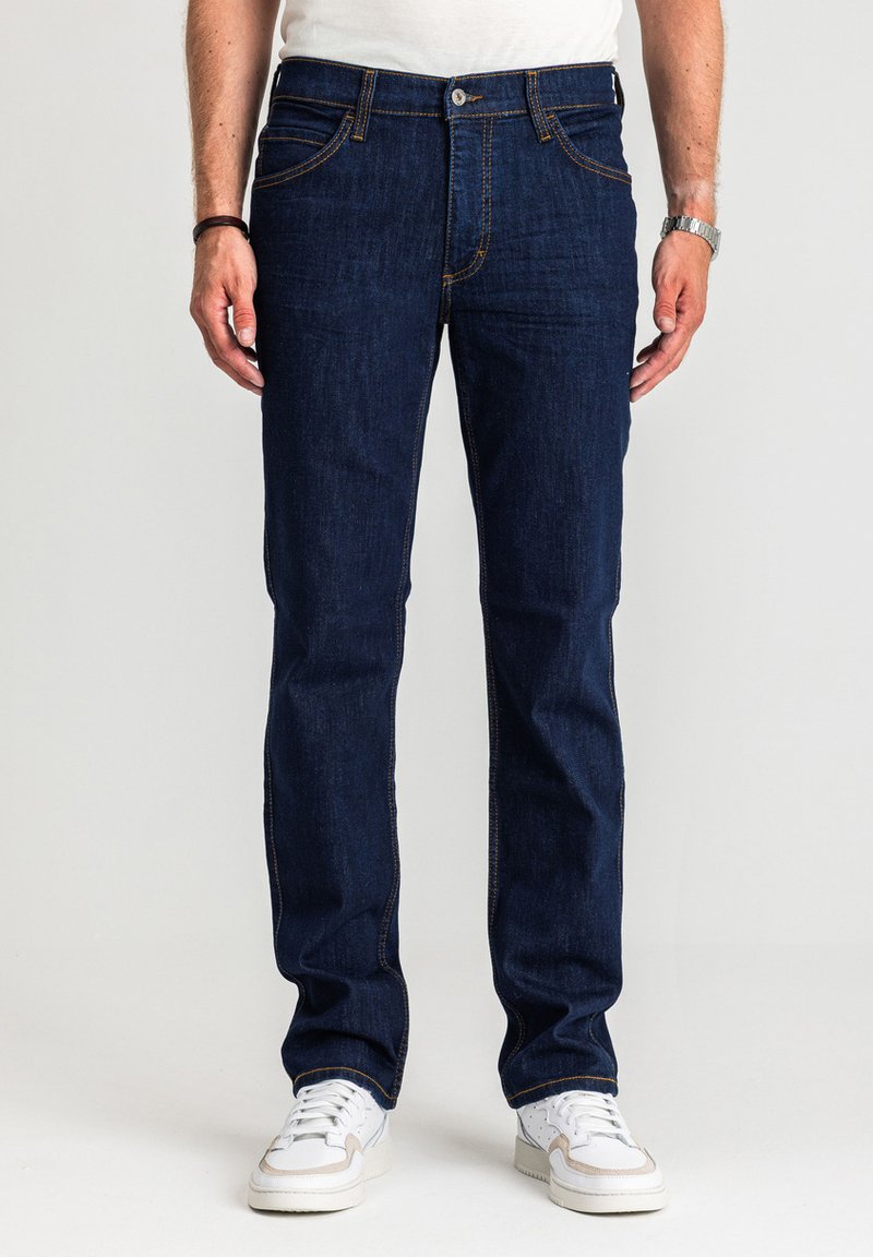 Ciemnoniebieskie dżinsy o prostym kroju, z pomarańczowymi przeszyciami i pięcioma kieszeniami, zestawione z białymi trampkami dla kontrastu.