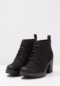 Svarta ankelstövlar med en texturerad ovandel, rund tå, snörning och en kraftig klack. Har dragflikar för enkel påtagning.