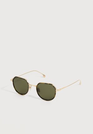 Lunettes de soleil octogonales avec montures en métal doré et verres vert foncé reposant sur une surface blanche.