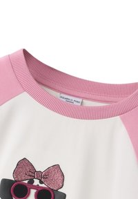 Roze raglanmouwen op een wit shirt kenmerken een glinsterende strik en een graphics van zonnebrillen. De stof lijkt zacht met een gladde textuur.