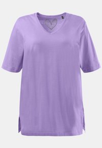 T-shirt violetta a maniche corte con scollo a V, texture morbida, vestibilità rilassata, presenta una sagoma a forma di cuore sul colletto e spacco laterale per facilità di movimento.