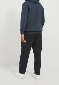 Granatowa bluza z kapturem z kieszenią kangurka, zestawiona z czarnymi luźnymi spodniami. Białe trampki dopełniają strój.