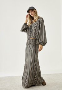 Top corto a rayas con mangas abullonadas y falda maxi a juego en tonos negro, beige y crema; presenta un detalle de lazo en el escote.