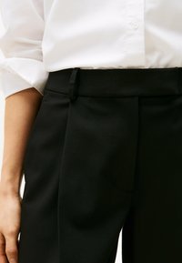 Zwarte op maat gemaakte broeken met een platte voorkant, riemlussen en een zachte textuur, gecombineerd met een witte knop-down overhemd.