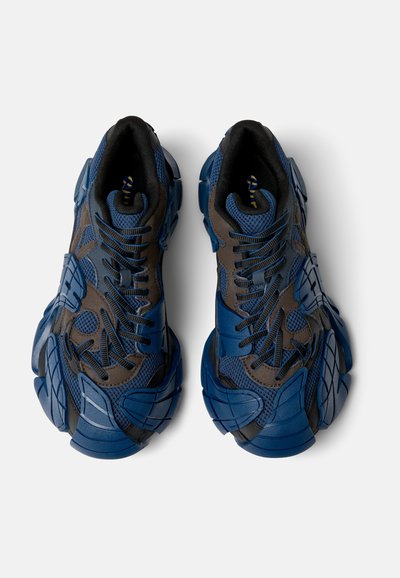 Blå och bruna sneakers med övre i mesh och syntetmaterial, texturerade överlägg och tjock gummisula. Har ett intrikat snörningssystem och uttalad häl.