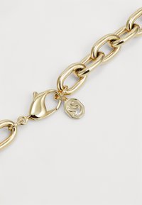Gold-colored chain bracelet featuring chunky, elongated links and a lobster clasp, adorned with a small charm displaying a logo.