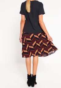 Una maglietta nera a maniche corte abbinata a una gonna plissettata multicolore a righe con motivi diagonali in rosso, arancione e blu navy.