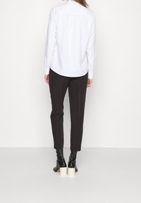 Chemise blanche à manches longues avec un ourlet arrondi, associée à un pantalon noir ajusté et des bottes noires à talon haut, avec un talon épais blanc.