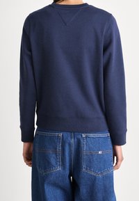Sudadera azul marino con puños y dobladillo acanalados, que presenta un detalle de cuello en forma de V. Combinada con jeans de denim azul de corte holgado con bolsillos.