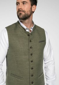 Olivgrüne Wollweste mit Mandarin-Kragen, Front mit sechs Knöpfen und zwei vorderen Taschen. Strukturierter Stoff mit dezentem Musterdetail.